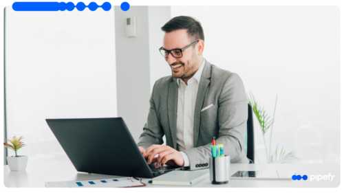 Smiling corporate professional in a suit and glasses working on a laptop at a bright office desk, applying effective ways to improve work performance
