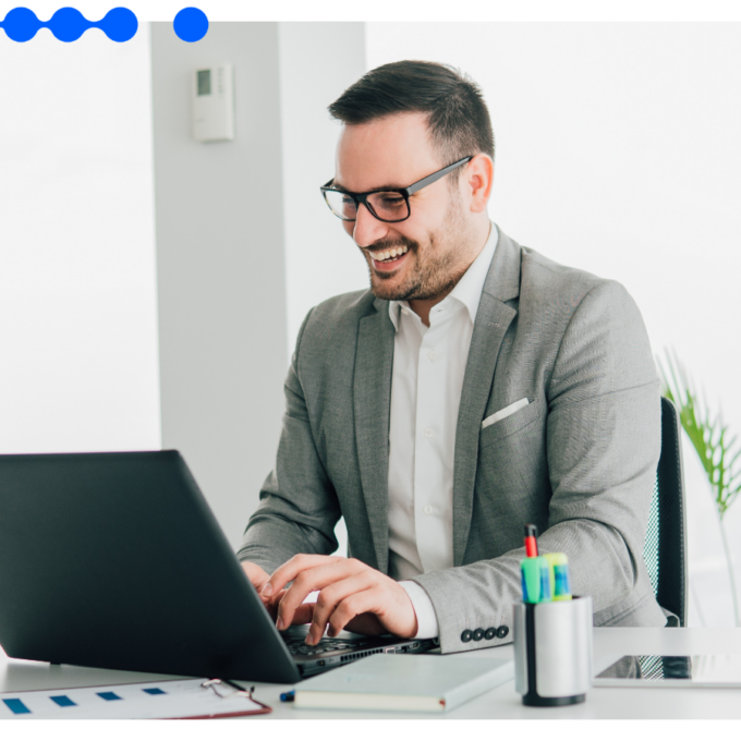 Smiling corporate professional in a suit and glasses working on a laptop at a bright office desk, applying effective ways to improve work performance