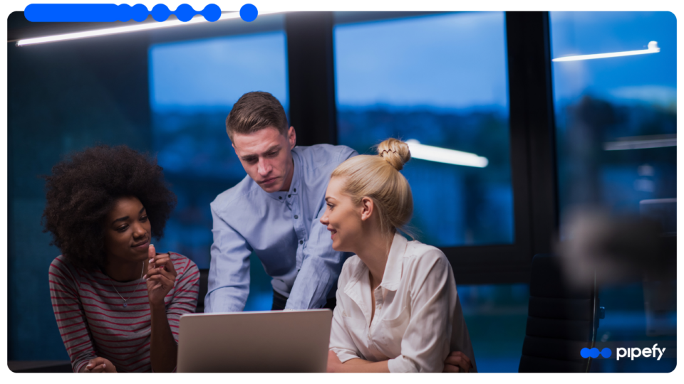Three diverse professionals collaborating around a laptop in a modern office setting, analyzing workflows and discussing strategies for process mapping