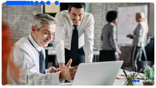 Dois profissionais analisam um laptop em um escritório movimentado, representando o dia a dia de um CRM para vendas com Agentes de IA