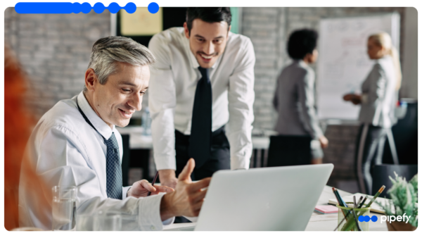 Dois profissionais analisam um laptop em um escritório movimentado, representando o dia a dia de um CRM para vendas com Agentes de IA