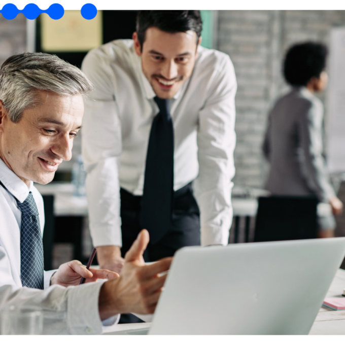 Dois profissionais analisam um laptop em um escritório movimentado, representando o dia a dia de um CRM para vendas com Agentes de IA