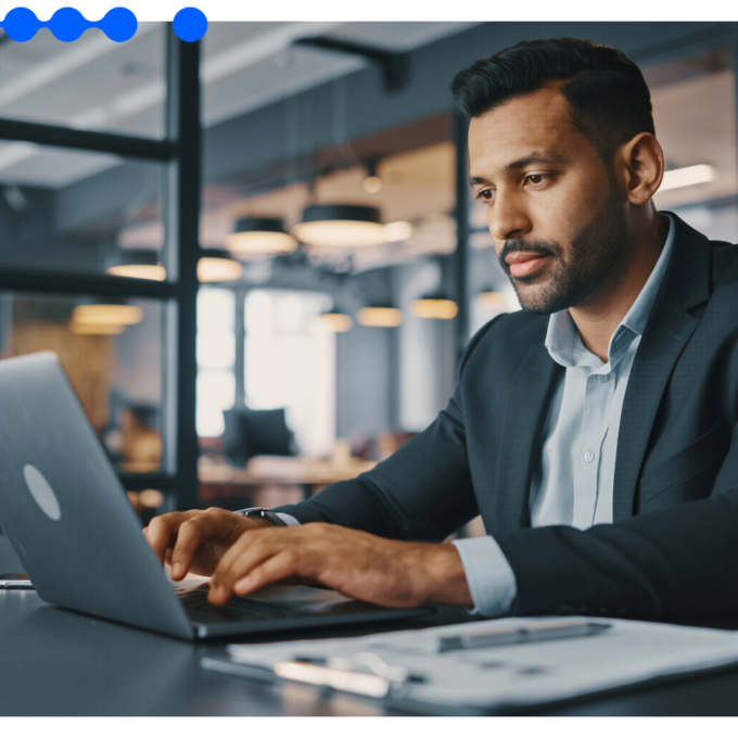 Homem executivo vestindo terno e camisa social trabalhando focado em um laptop em um escritório moderno, com papéis sobre a mesa, organizando o processo de vendas