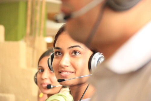 Mulher usa headphone típico de atendimento ao cliente em meio a outros profissionais em um call center