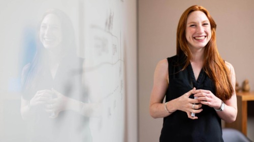 smiling woman with red hair standing in front of a dry-erase board