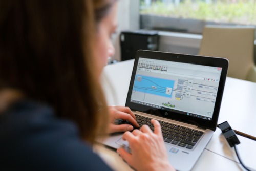 Photo taken from over the shoulder of a female-appearing person who is working on a laptop computer inside an office space..