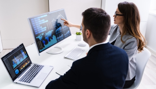 Um homem e uma mulher olhando para gráficos em dois computadores.