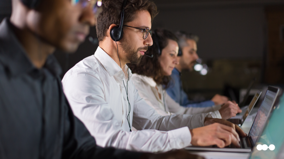 Customer support agents wearing headsets and working on laptops in a service operations room