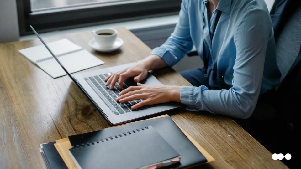Professional using an employee portal on a laptop at a desk, surrounded by notebooks and a coffee cup