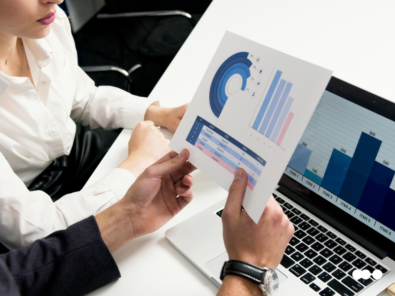 Team members reviewing a printed report with KPIs and FTE performance charts, alongside a dashboard on a laptop.