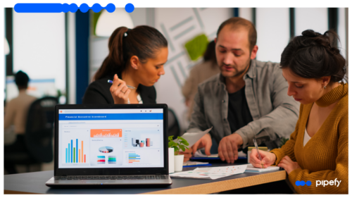 Equipe analisando dashboards financeiros em notebook, com gráficos e relatórios sobre a mesa, durante reunião de revisão da esteira de crédito