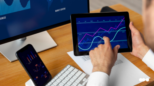Financial services trends illustrated by a digital candlestick chart with buy and sell signals, over a businessperson using a tablet