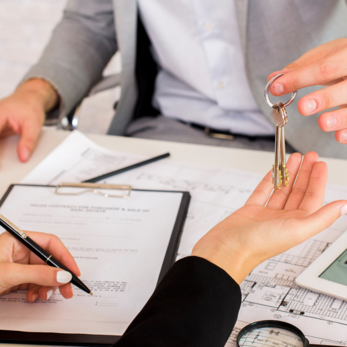 A successful real estate closing with keys being exchanged over a desk with blueprints and a contract, the result of a streamlined property intake