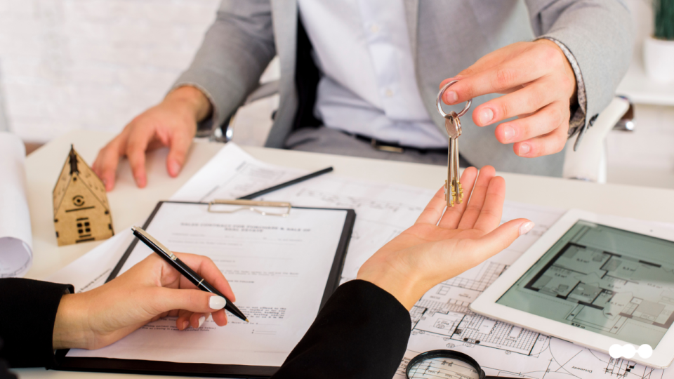 A successful real estate closing with keys being exchanged over a desk with blueprints and a contract, the result of a streamlined property intake