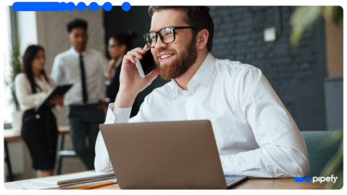 Profissional sorri ao telefone diante do laptop, conduzindo o processo comercial de ponta a ponta no CRM AI Studio do Pipefy