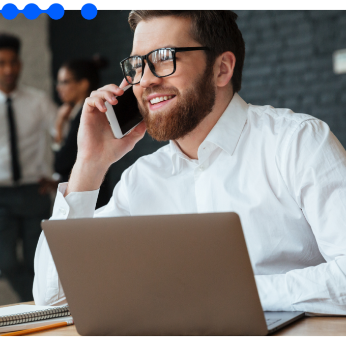Profissional sorri ao telefone diante do laptop, conduzindo o processo comercial de ponta a ponta no CRM AI Studio do Pipefy