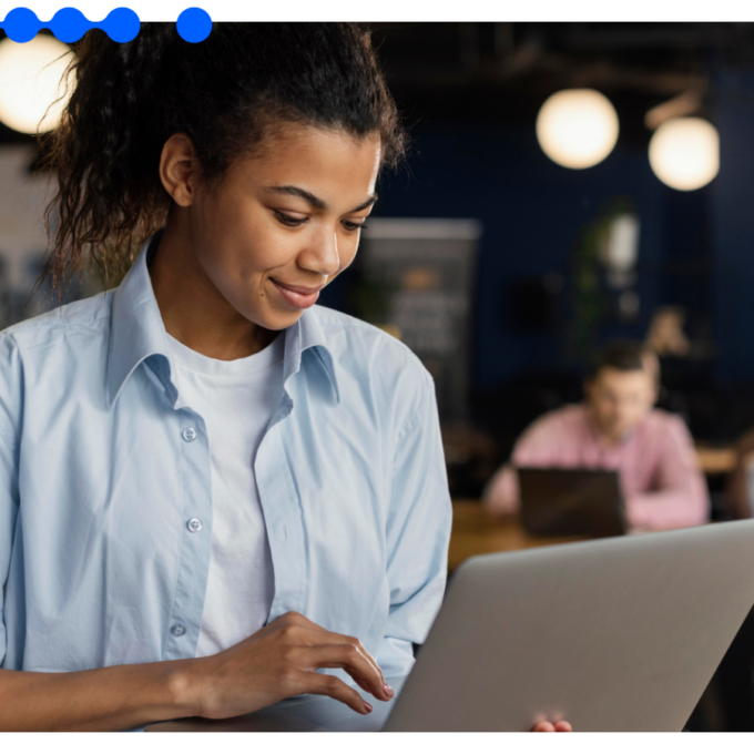 Mulher jovem trabalhando em um laptop em um ambiente de escritório colaborativo.