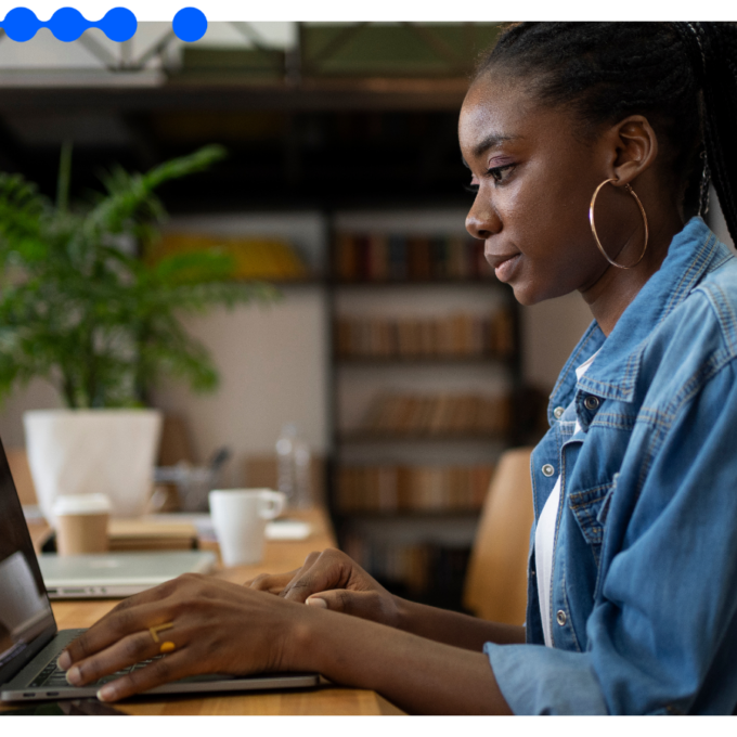 Mulher trabalhando em um laptop em ambiente de escritório, concentrada na tela, com estante de livros ao fundo e logotipo da Pipefy no canto inferior direito