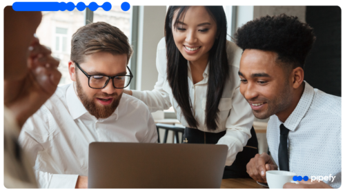 Três profissionais em um escritório moderno, sorrindo e colaborando ao redor de um laptop, simbolizando a busca por eficiência operacional com IA em seus processos internos