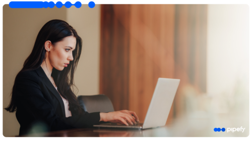 Young professional woman with long dark hair and a black blazer focused while working on a silver laptop at a wooden table, symbolizing the application of Embedded AI in business process orchestration