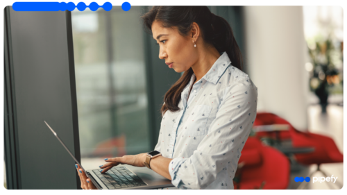 Focused professional woman in a light-colored patterned shirt looking intently at a laptop screen in a modern office with red chairs, researching how to automate hiring process