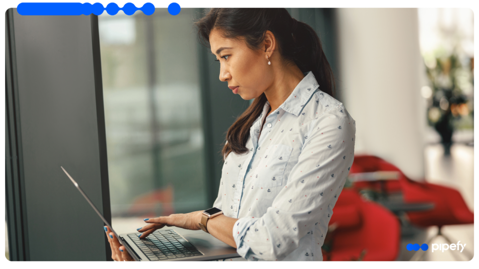 Focused professional woman in a light-colored patterned shirt looking intently at a laptop screen in a modern office with red chairs, researching how to automate hiring process