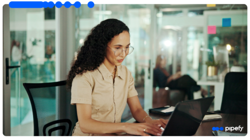 Mulher de cabelos cacheados e óculos trabalhando concentrada em um notebook em um escritório corporativo para estruturar um fluxo de marketing