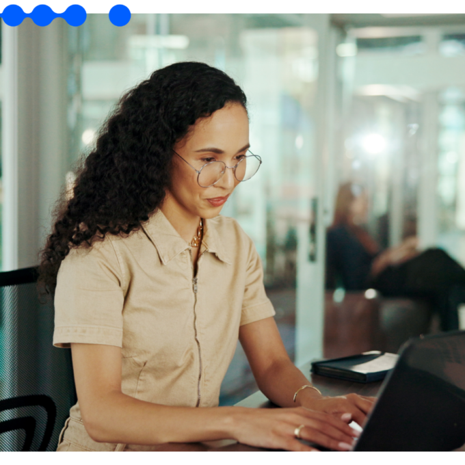 Mulher de cabelos cacheados e óculos trabalhando concentrada em um notebook em um escritório corporativo para estruturar um fluxo de marketing