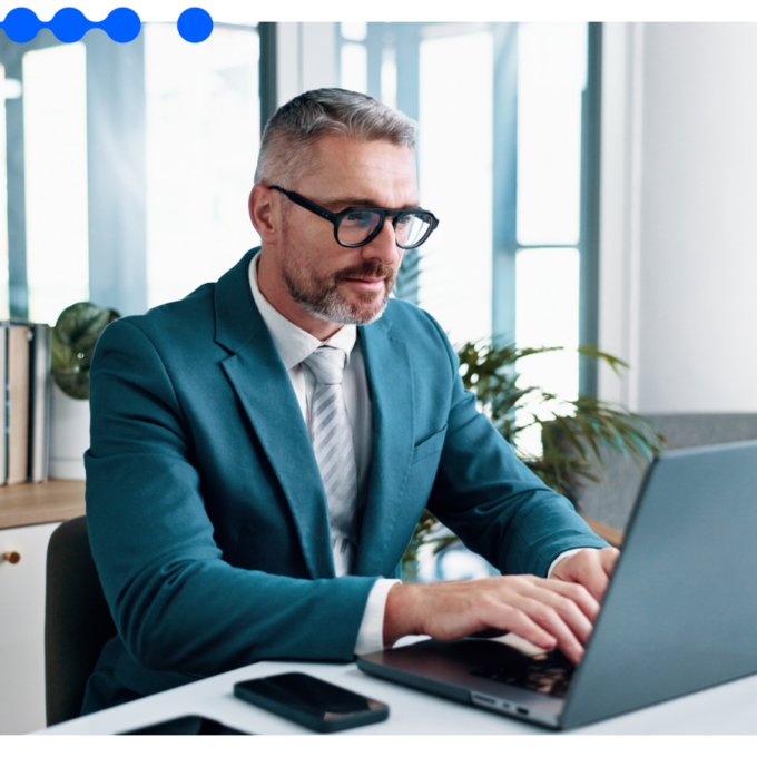 Homem de negócios grisalho de óculos e terno trabalhando em um laptop em um escritório moderno, realizando atividades em um processo de background check