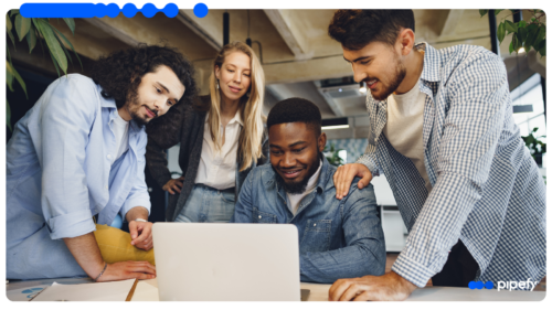 Equipe reunida em escritório moderno colaborando e olhando para um laptop, utilizando uma ferramenta de gestão de tarefas para organizar o trabalho