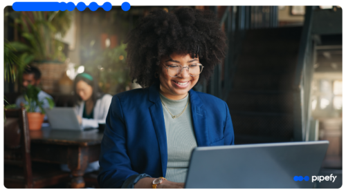 Smiling professional woman with glasses and curly hair working on a laptop in a modern office, representing effective Supplier Risk Management