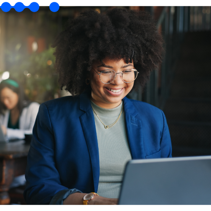 Smiling professional woman with glasses and curly hair working on a laptop in a modern office, representing effective Supplier Risk Management