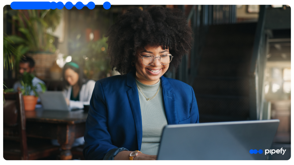 Smiling professional woman with glasses and curly hair working on a laptop in a modern office, representing effective Supplier Risk Management