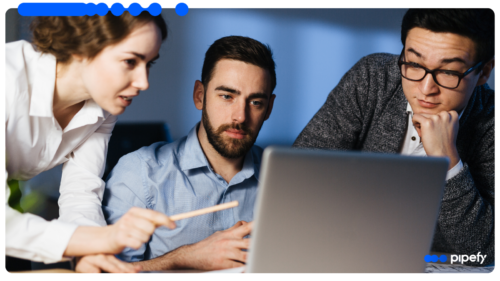 Three focused professionals working together in a corporate office, with a woman pointing at a laptop screen while analyzing shared services workflows data
