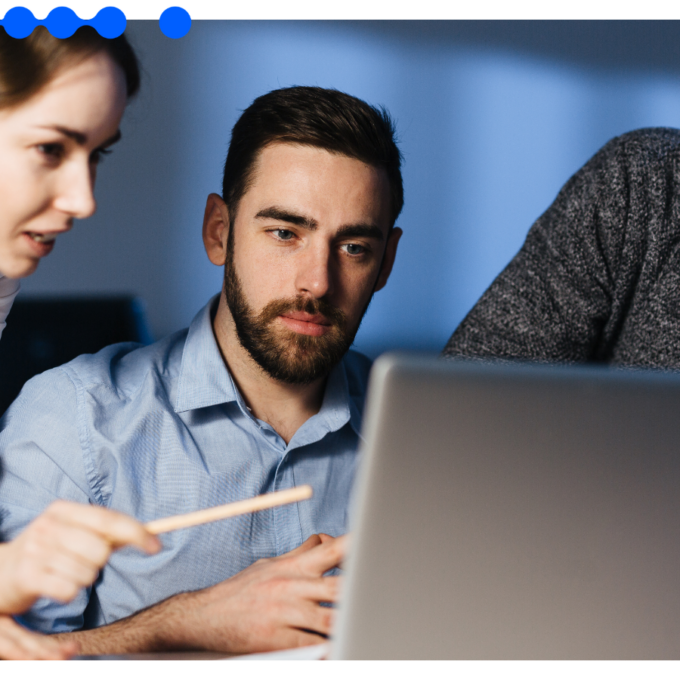 Three focused professionals working together in a corporate office, with a woman pointing at a laptop screen while analyzing shared services workflows data