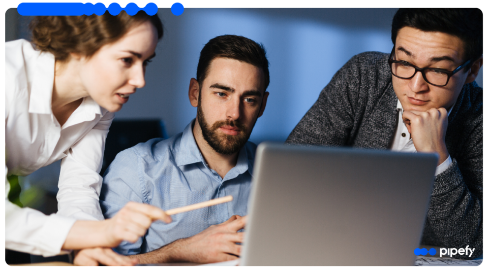 Three focused professionals working together in a corporate office, with a woman pointing at a laptop screen while analyzing shared services workflows data