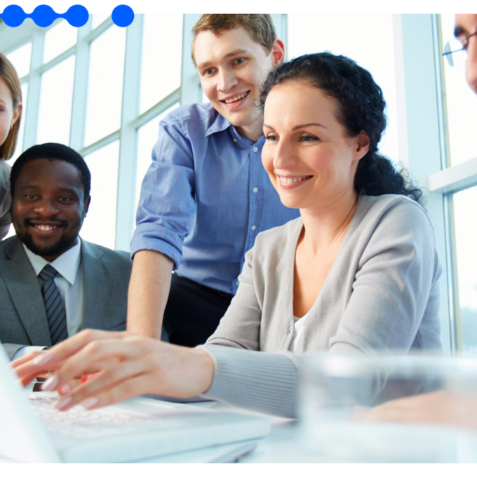 Grupo de cinco profissionais sorridentes reunidos ao redor de uma mesa em um escritório moderno e iluminado, olhando juntos para a tela de um laptop branco enquanto colaboram usando tecnologia low-code