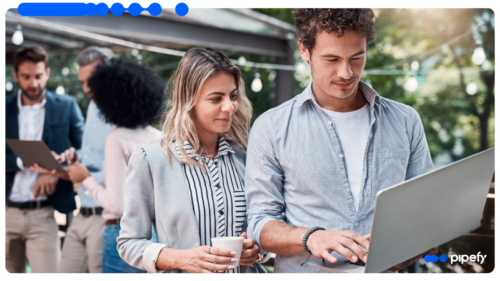 Equipe técnica revisa decisões em laptop enquanto outros profissionais colaboram ao fundo, ilustrando o ofício por trás de uma plataforma de IA empresarial