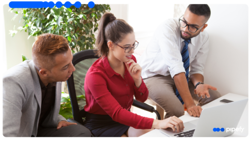 Três profissionais reunidos em torno de um laptop em um escritório moderno, analisando a operação comercial com um CRM com IA