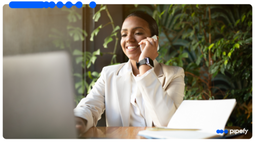 Mulher de negócios sorri ao telefone em frente ao laptop, ilustrando o que é CRM na rotina de vendas B2B