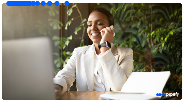 Mulher de negócios sorri ao telefone em frente ao laptop, ilustrando o que é CRM na rotina de vendas B2B