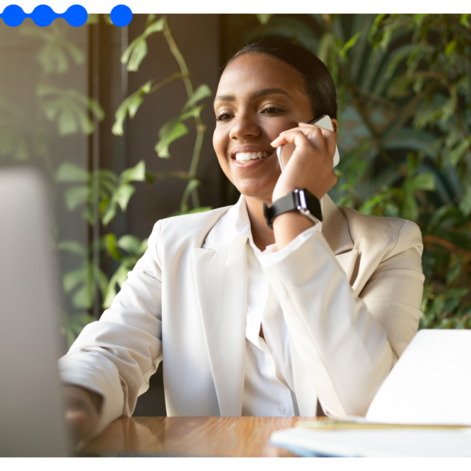 Mulher de negócios sorri ao telefone em frente ao laptop, ilustrando o que é CRM na rotina de vendas B2B