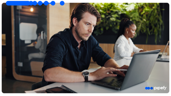 A male professional, focused on embedded B2B credit operations, works on a laptop in a modern office as a colleague works behind him