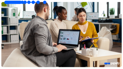 A team of three professionals reviews data dashboards on a laptop while discussing procurement orchestration in a modern office