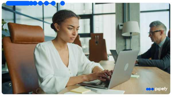 A professional works on a laptop in a modern office as a colleague works nearby, reflecting the everyday, ungoverned AI use that defines shadow AI