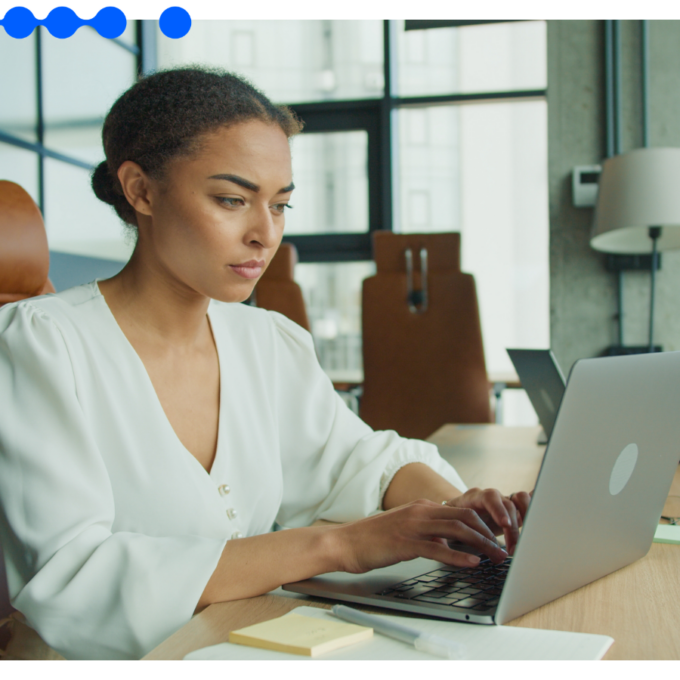 A professional works on a laptop in a modern office as a colleague works nearby, reflecting the everyday, ungoverned AI use that defines shadow AI