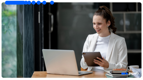 Profissional sorridente gerenciando a operação em um software de CRM com tablet ao lado do notebook em um escritório moderno