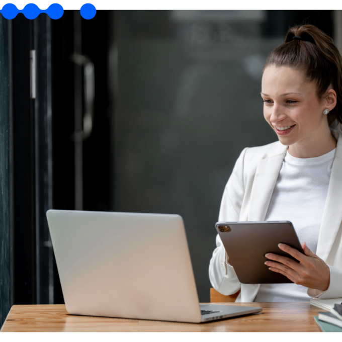 Profissional sorridente gerenciando a operação em um software de CRM com tablet ao lado do notebook em um escritório moderno