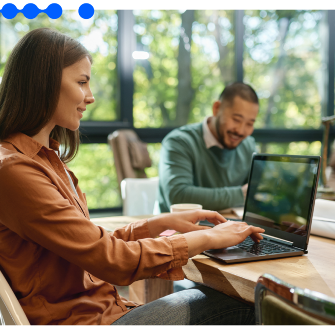 Two IT professionals work on laptops in a modern office, illustrating an IT modernization strategy that orchestrates systems on top of existing tools